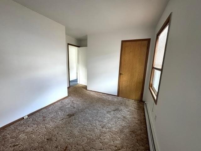 unfurnished bedroom with a baseboard heating unit, baseboards, and carpet floors