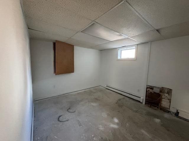 basement featuring a paneled ceiling and baseboard heating