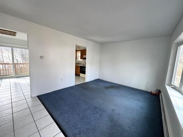 spare room featuring a baseboard heating unit, plenty of natural light, light tile patterned flooring, and visible vents