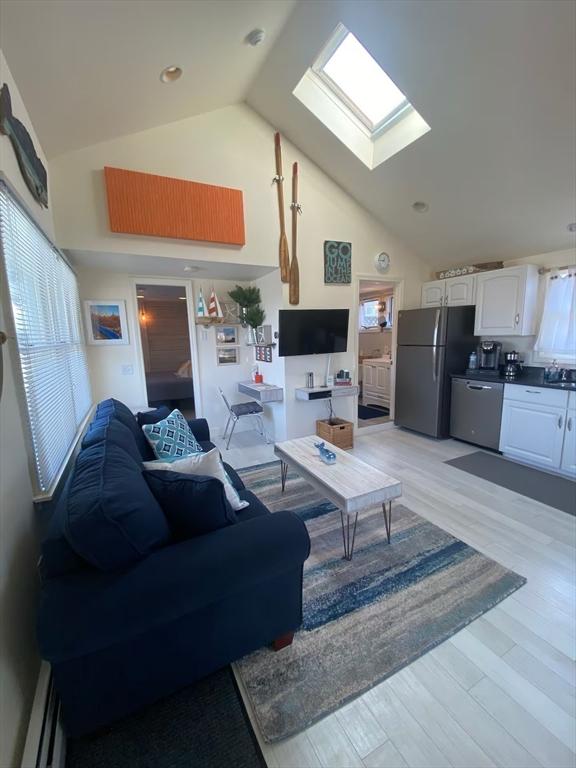 living room featuring a skylight, sink, baseboard heating, high vaulted ceiling, and light wood-type flooring