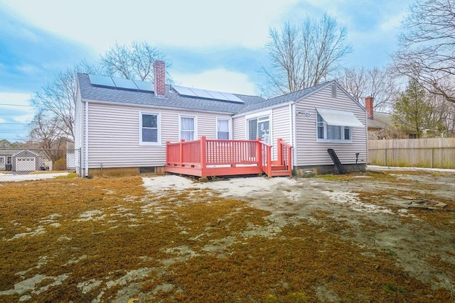 back of house featuring solar panels, a shingled roof, fence, a wooden deck, and a chimney