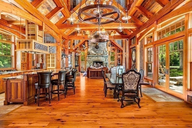 dining room featuring beam ceiling, french doors, high vaulted ceiling, a fireplace, and light wood-type flooring