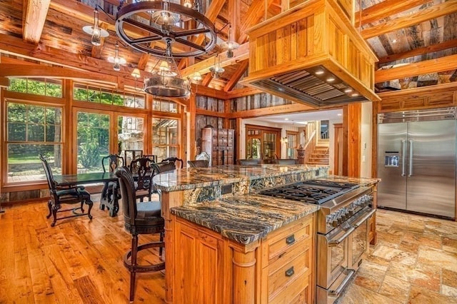 kitchen with custom exhaust hood, premium appliances, beam ceiling, high vaulted ceiling, and dark stone countertops