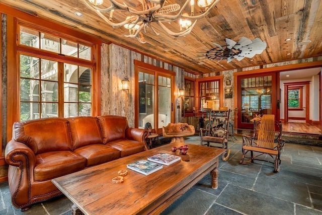 interior space with ceiling fan with notable chandelier, wooden ceiling, and wood walls