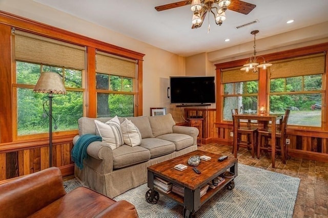 living room with hardwood / wood-style floors, ceiling fan with notable chandelier, and wood walls