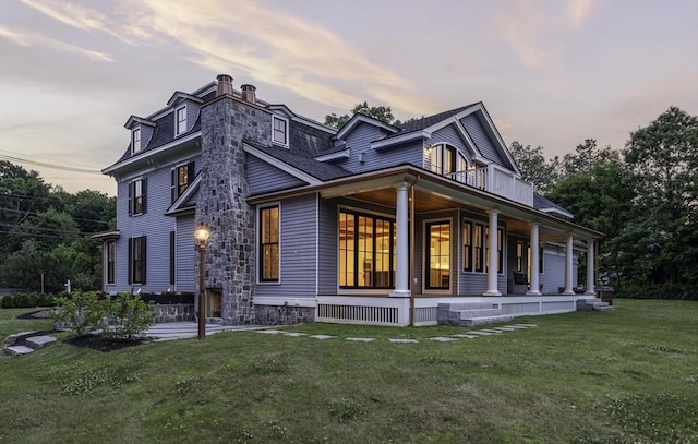 property exterior at dusk with covered porch and a lawn