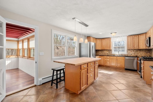 kitchen with a sink, baseboard heating, appliances with stainless steel finishes, backsplash, and a center island