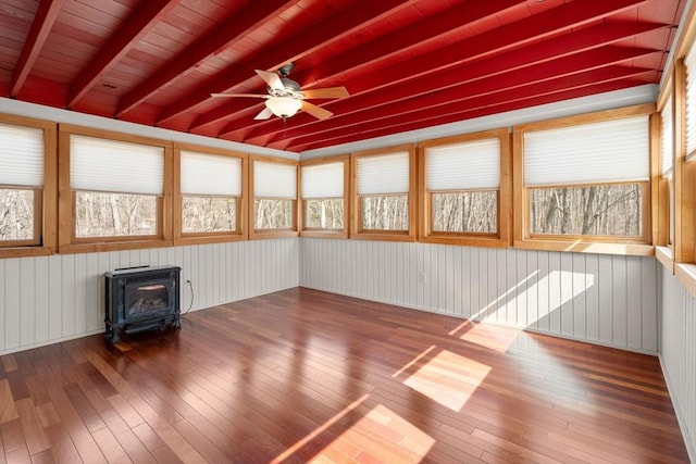 spare room featuring beam ceiling, a wood stove, a ceiling fan, and hardwood / wood-style floors