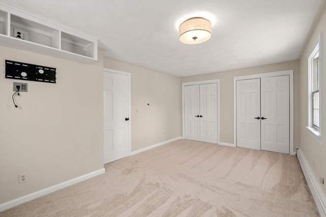 unfurnished bedroom featuring baseboards, multiple closets, carpet flooring, and a baseboard radiator