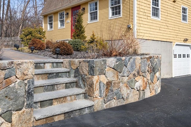 exterior space featuring an attached garage, fence, driveway, and a shingled roof