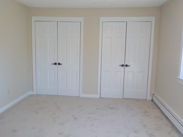 unfurnished bedroom featuring baseboards, two closets, carpet, and a baseboard radiator