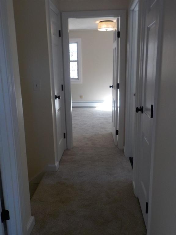 hall featuring a baseboard heating unit, light colored carpet, and baseboards