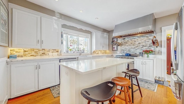 kitchen with white cabinets, light hardwood / wood-style floors, wall chimney exhaust hood, and a kitchen bar