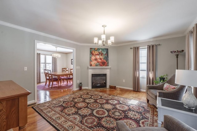 living room with a notable chandelier, light wood-style flooring, ornamental molding, a glass covered fireplace, and baseboards