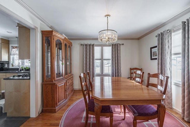 dining area with ornamental molding, baseboards, a notable chandelier, and light wood finished floors