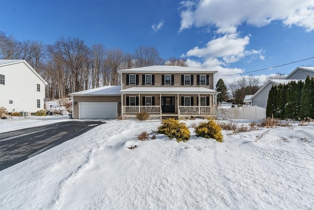 colonial inspired home with covered porch, driveway, an attached garage, and central AC unit