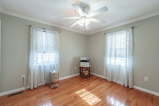 spare room with crown molding, light wood finished floors, visible vents, and baseboards