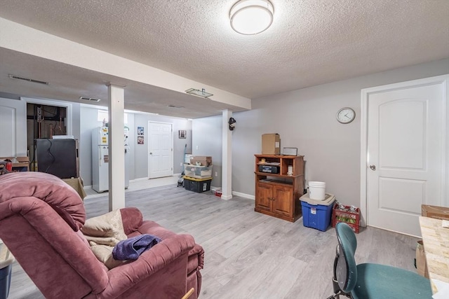 living area with baseboards, visible vents, light wood-style flooring, and a textured ceiling