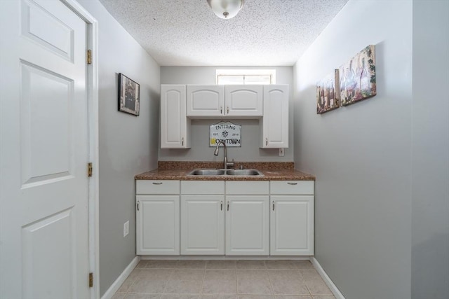 kitchen with dark countertops, white cabinetry, a sink, a textured ceiling, and baseboards