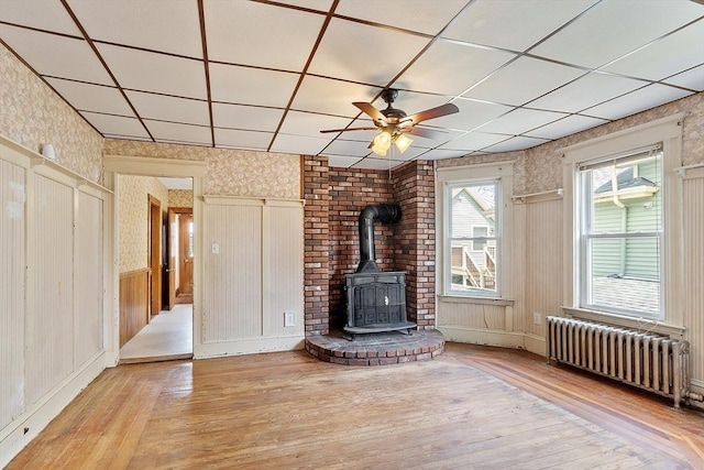 49-51 Fairmount Ave, Somerville, MA 02144 - unfurnished living room featuring radiator, wallpapered walls, a wood stove, hardwood / wood-style flooring, and a ceiling fan