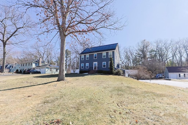 colonial-style house featuring solar panels, a front lawn, and an outdoor structure