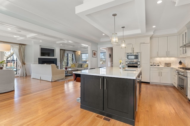 kitchen featuring white cabinets, light hardwood / wood-style flooring, decorative light fixtures, stainless steel appliances, and a kitchen island with sink