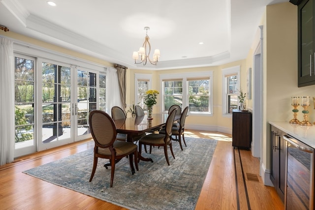 dining space with a healthy amount of sunlight, a notable chandelier, light hardwood / wood-style flooring, and a raised ceiling