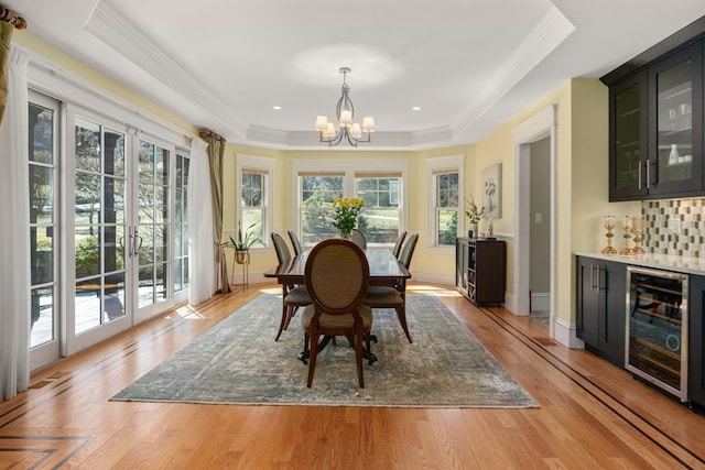 dining area featuring a tray ceiling, light hardwood / wood-style flooring, wine cooler, and a notable chandelier