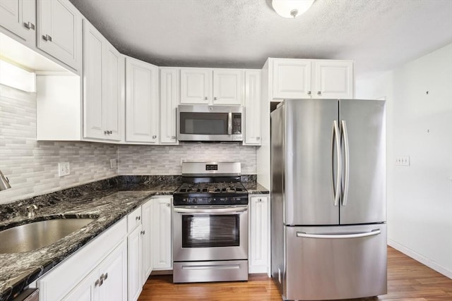 kitchen featuring light wood-type flooring, dark stone counters, stainless steel appliances, and white cabinetry