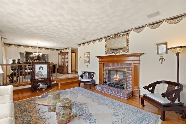 living room with visible vents, a brick fireplace, a chandelier, wood finished floors, and a textured ceiling