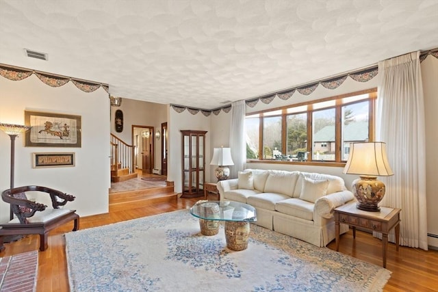 living room featuring visible vents, a textured ceiling, wood finished floors, and stairs