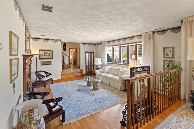 living area featuring visible vents, a textured ceiling, wood finished floors, baseboard heating, and stairs