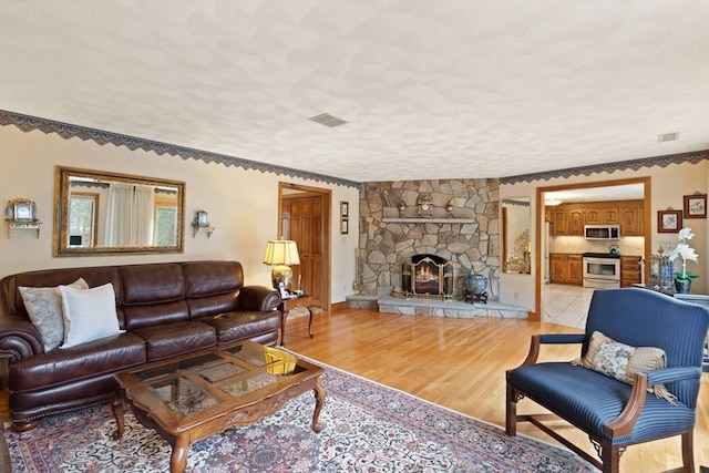 living room featuring visible vents, a textured ceiling, a stone fireplace, and light wood-style floors