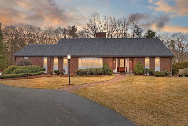 ranch-style home with brick siding, a chimney, a yard, and a shingled roof