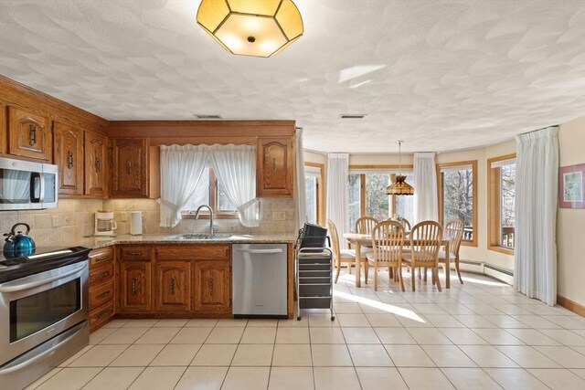 kitchen featuring a healthy amount of sunlight, light stone countertops, brown cabinetry, a sink, and appliances with stainless steel finishes