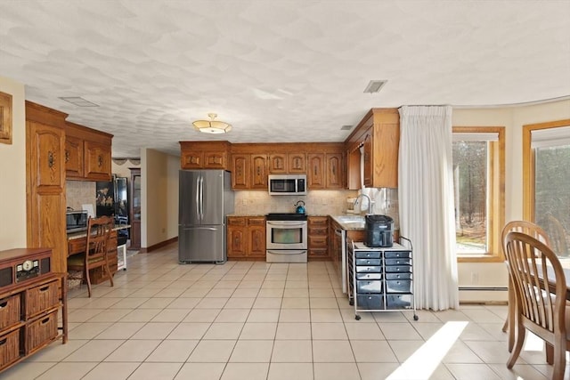 kitchen featuring light tile patterned floors, decorative backsplash, brown cabinets, baseboard heating, and stainless steel appliances