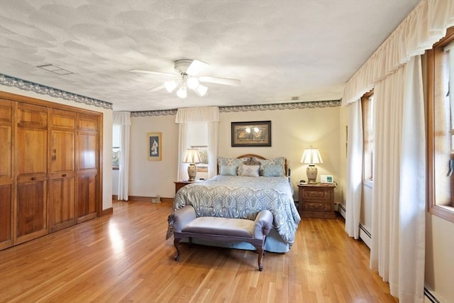 bedroom featuring a baseboard heating unit, light wood-style flooring, baseboards, and baseboard heating