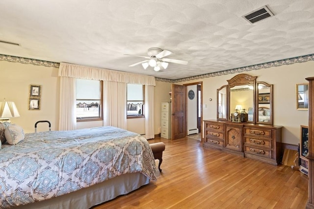 bedroom featuring baseboard heating, visible vents, light wood finished floors, and a textured ceiling