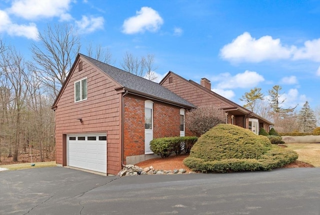 view of property exterior featuring brick siding, aphalt driveway, roof with shingles, a chimney, and an attached garage