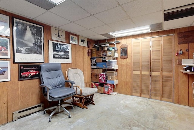 living area featuring a baseboard radiator, a paneled ceiling, unfinished concrete flooring, and wood walls