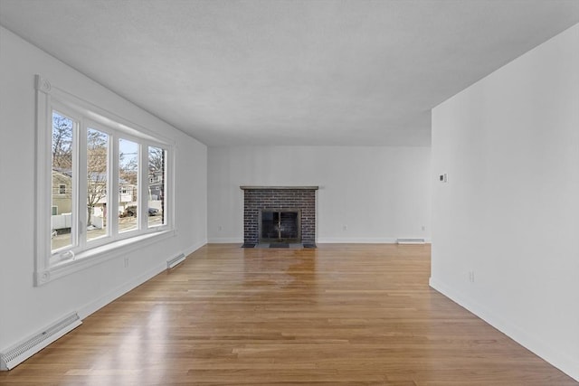 unfurnished living room with a brick fireplace, a baseboard heating unit, and light hardwood / wood-style flooring