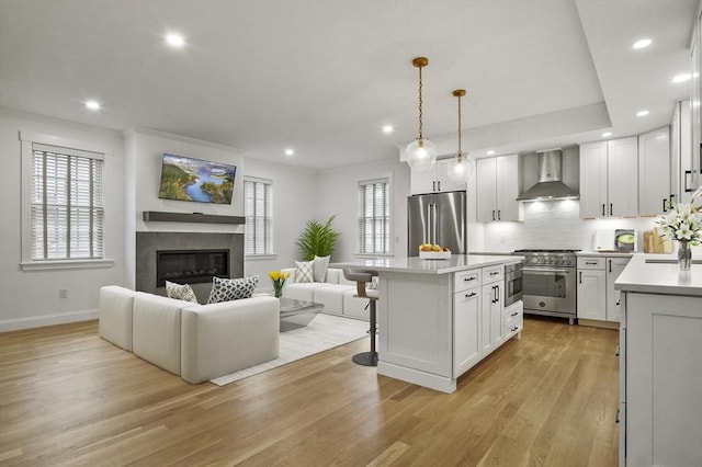140 Main St Unit E, Amesbury, MA 01913 - kitchen with wall chimney exhaust hood, stainless steel appliances, open floor plan, light wood-type flooring, and a breakfast bar area