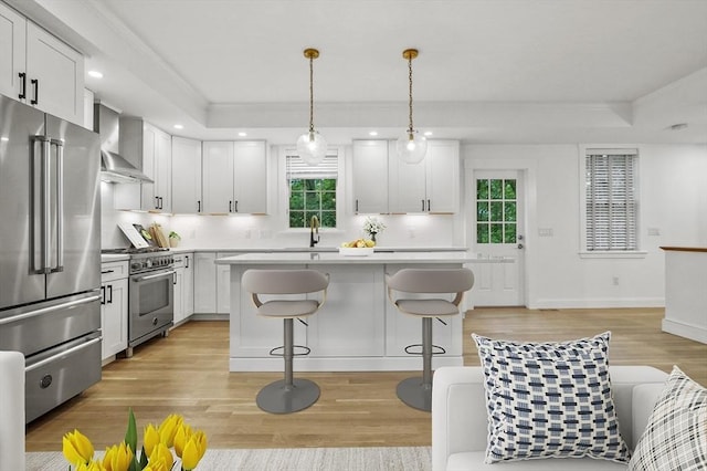 140 Main St Unit E, Amesbury, MA 01913 - kitchen with high quality appliances, wall chimney exhaust hood, light wood-style flooring, a kitchen breakfast bar, and white cabinetry