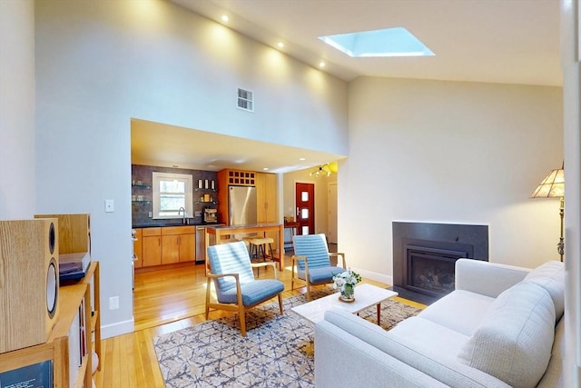 living room with recessed lighting, a fireplace with flush hearth, visible vents, light wood-style flooring, and a skylight