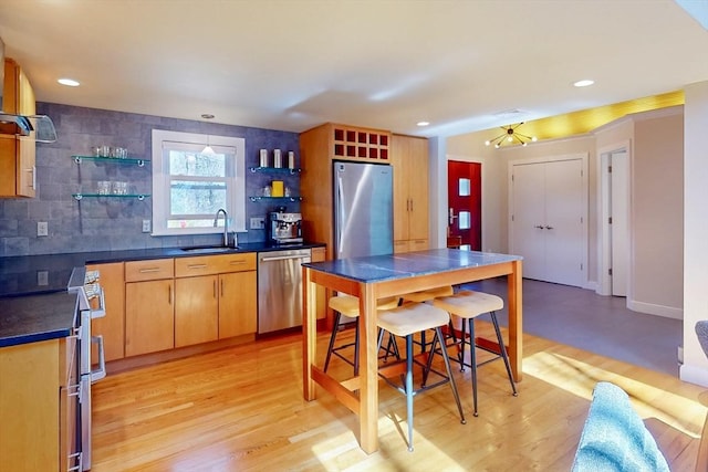kitchen with open shelves, light wood-style floors, appliances with stainless steel finishes, dark countertops, and a sink