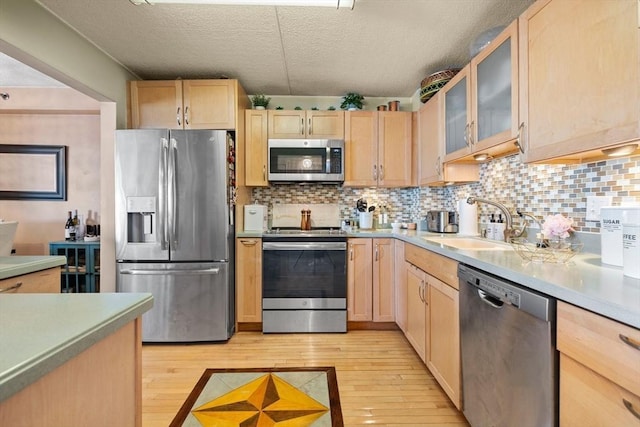 kitchen with light brown cabinets, a sink, tasteful backsplash, stainless steel appliances, and light wood finished floors