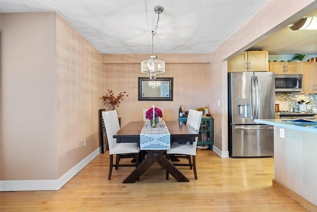 dining space with a textured ceiling, baseboards, a notable chandelier, and light wood finished floors