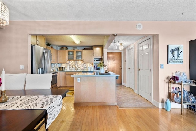 kitchen with tasteful backsplash, light brown cabinets, light countertops, appliances with stainless steel finishes, and light wood-style floors