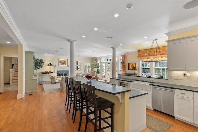 kitchen with dark countertops, open floor plan, stainless steel dishwasher, ornate columns, and a sink