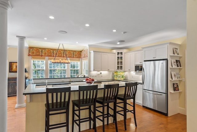 kitchen with ornate columns, a center island with sink, crown molding, and freestanding refrigerator